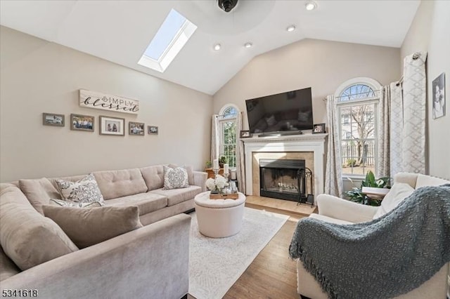 living area featuring high vaulted ceiling, a skylight, wood finished floors, and a premium fireplace