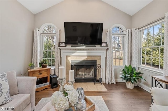 living area with lofted ceiling, baseboards, a tiled fireplace, and wood finished floors