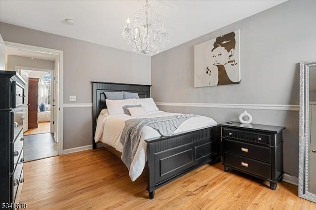 bedroom with an inviting chandelier, light wood-style flooring, and baseboards