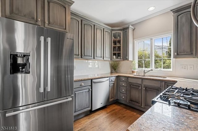 kitchen featuring dark wood-style flooring, a sink, light stone countertops, stainless steel appliances, and backsplash