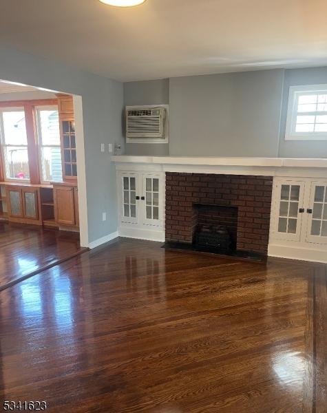 unfurnished living room with a wall unit AC, a brick fireplace, wood finished floors, and baseboards