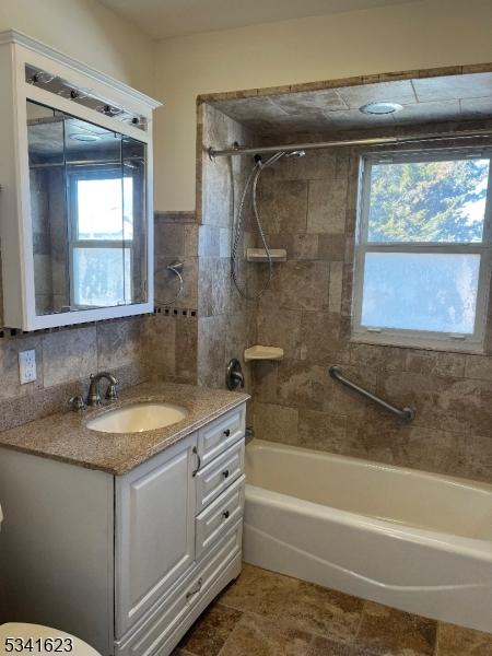 full bath featuring a wealth of natural light, vanity, tile walls, and washtub / shower combination