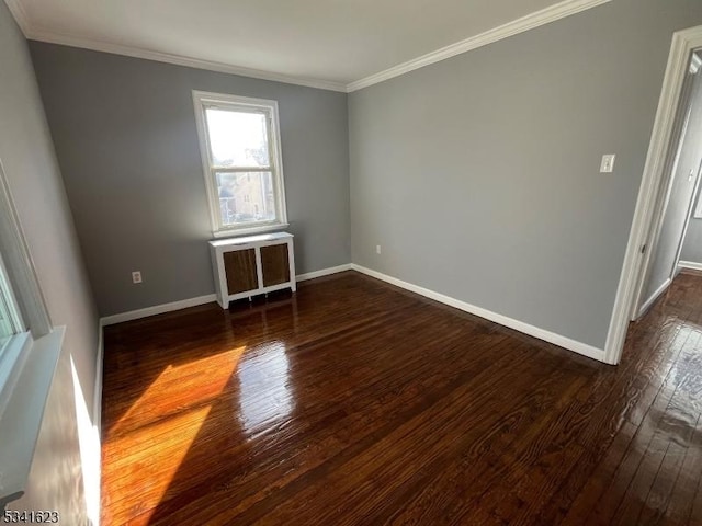 empty room with dark wood finished floors, radiator, crown molding, and baseboards