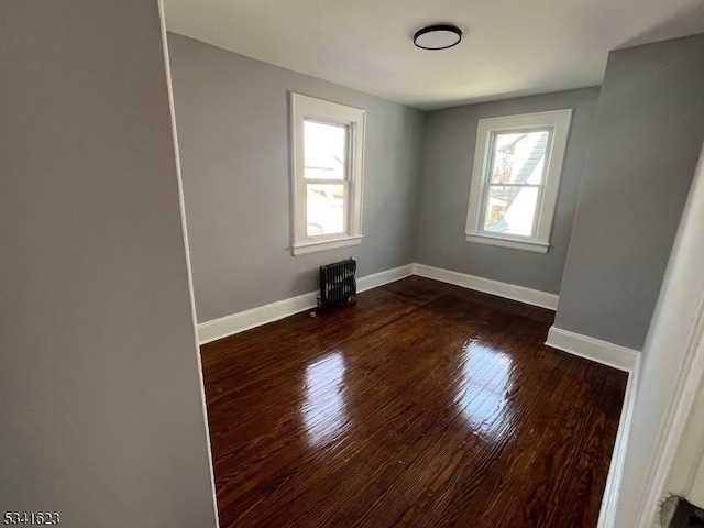 spare room featuring dark wood-style flooring, radiator, baseboards, and a wealth of natural light