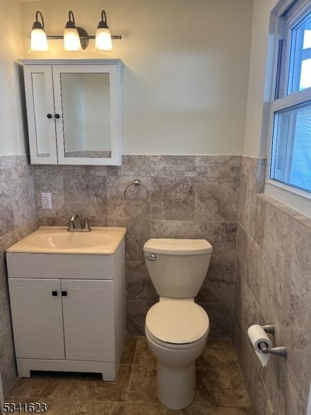 bathroom with a wainscoted wall, toilet, tile walls, and vanity