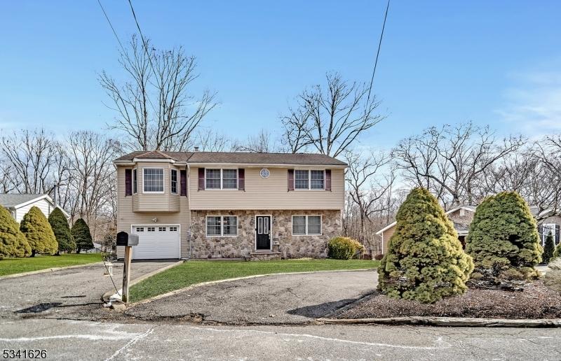 colonial-style house with a garage, stone siding, aphalt driveway, and a front lawn