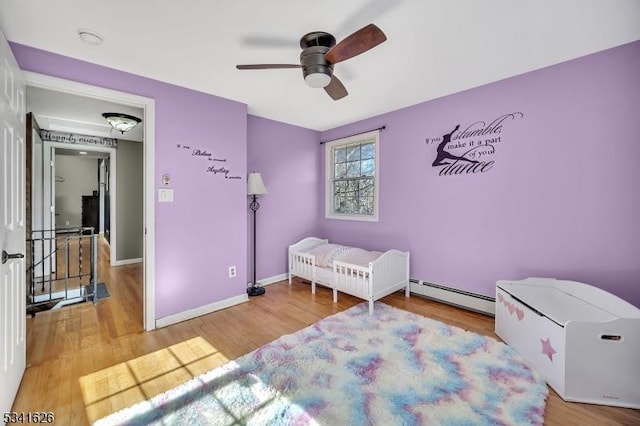 bedroom featuring a baseboard heating unit, ceiling fan, wood finished floors, and baseboards