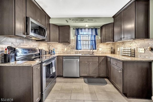 kitchen featuring dark brown cabinetry, appliances with stainless steel finishes, light stone counters, and a sink