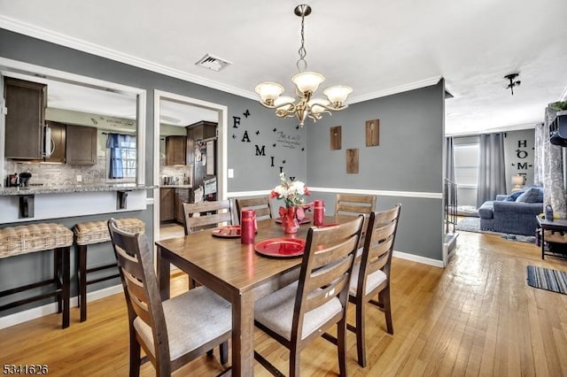 dining room featuring crown molding, visible vents, baseboards, light wood-type flooring, and an inviting chandelier