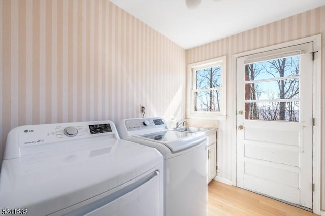 laundry room with wallpapered walls, cabinet space, light wood-style floors, washing machine and dryer, and a sink