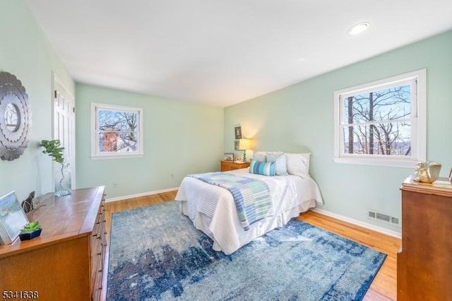 bedroom featuring baseboards, multiple windows, visible vents, and wood finished floors