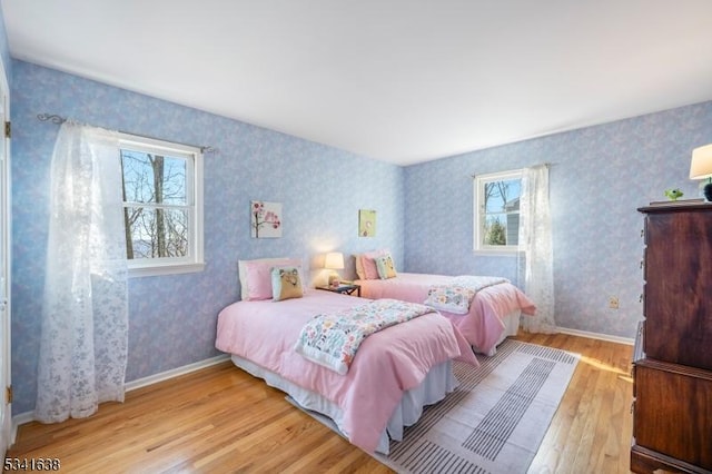 bedroom featuring wood finished floors, baseboards, and wallpapered walls