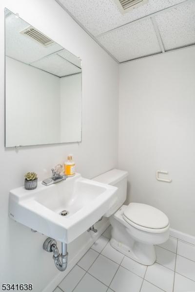 half bathroom featuring baseboards, a drop ceiling, toilet, and tile patterned floors