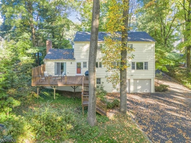 back of property featuring driveway, a chimney, an attached garage, stairs, and a deck