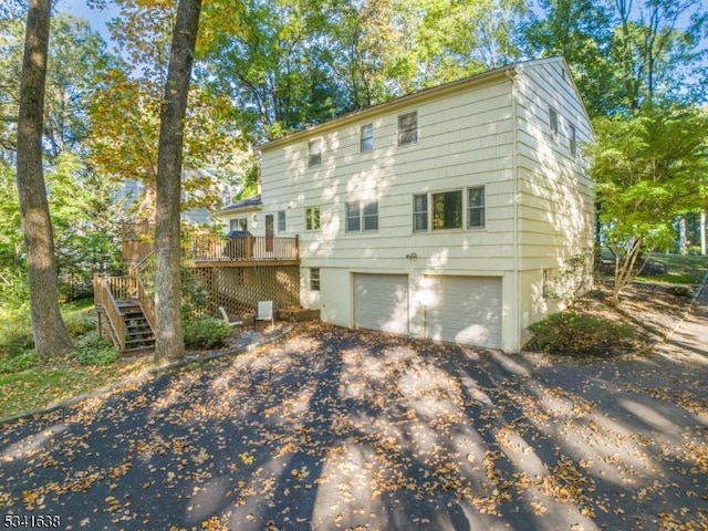 rear view of house featuring aphalt driveway, stairway, a garage, and a deck