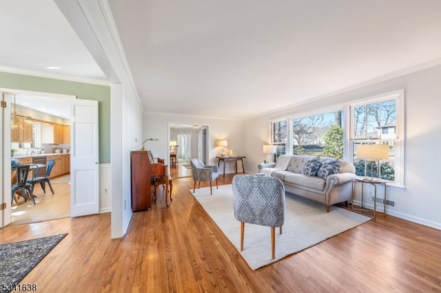 living area featuring ornamental molding, baseboards, and light wood finished floors