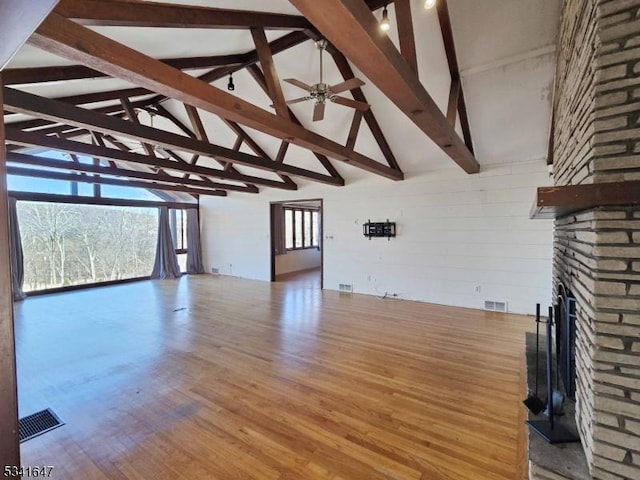 unfurnished living room featuring a ceiling fan, visible vents, a stone fireplace, and wood finished floors