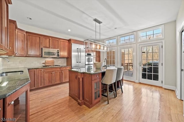 kitchen with tasteful backsplash, appliances with stainless steel finishes, brown cabinets, light wood-style floors, and a sink