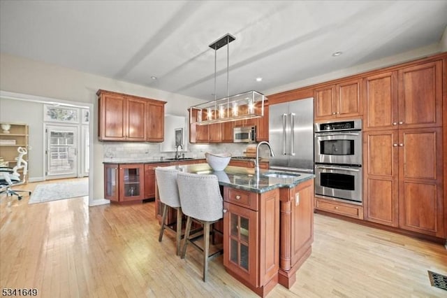 kitchen with stainless steel appliances, brown cabinets, a sink, and an island with sink