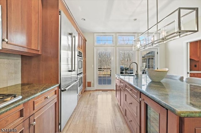 kitchen featuring a sink, light wood-type flooring, brown cabinets, tasteful backsplash, and a center island with sink