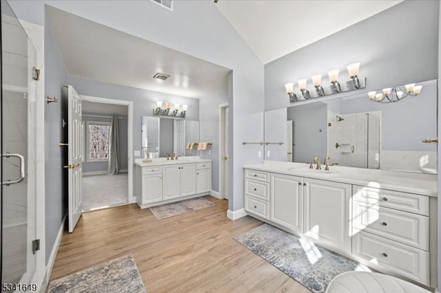 bathroom featuring wood finished floors, two vanities, a sink, vaulted ceiling, and a shower stall