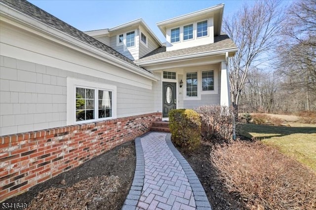 view of exterior entry with roof with shingles and brick siding