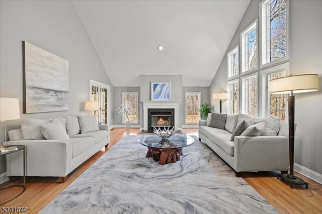 living room with a fireplace with flush hearth, high vaulted ceiling, baseboards, and wood finished floors