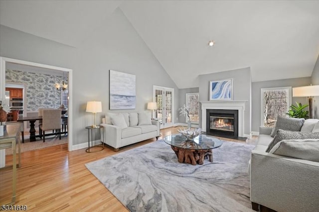 living room featuring a fireplace with flush hearth, high vaulted ceiling, wood finished floors, and baseboards