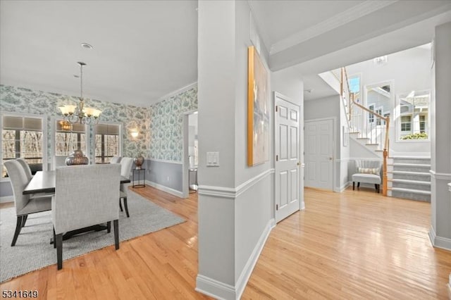 dining space with wood finished floors, stairs, ornamental molding, wallpapered walls, and an inviting chandelier