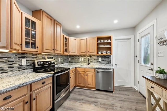 kitchen with light stone counters, light wood finished floors, open shelves, appliances with stainless steel finishes, and a sink