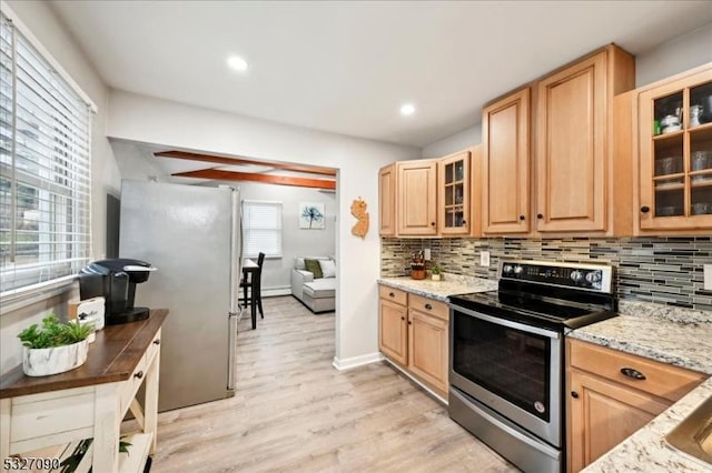 kitchen with light brown cabinets, light wood-style flooring, appliances with stainless steel finishes, decorative backsplash, and glass insert cabinets