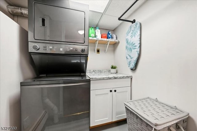 interior space featuring light stone countertops, a paneled ceiling, stacked washing maching and dryer, white cabinetry, and open shelves