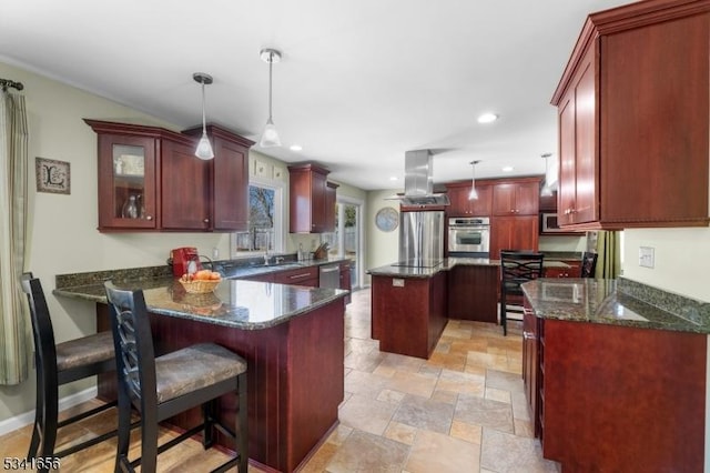 kitchen with dark stone counters, a peninsula, island exhaust hood, stainless steel appliances, and dark brown cabinets