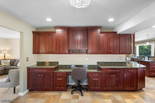 kitchen with reddish brown cabinets, baseboards, dark stone counters, built in study area, and recessed lighting