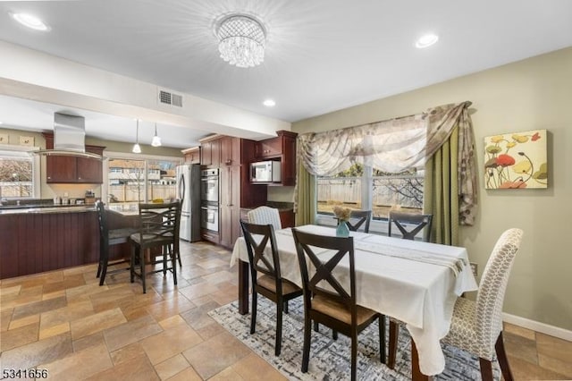 dining space featuring baseboards, visible vents, a chandelier, and stone tile flooring