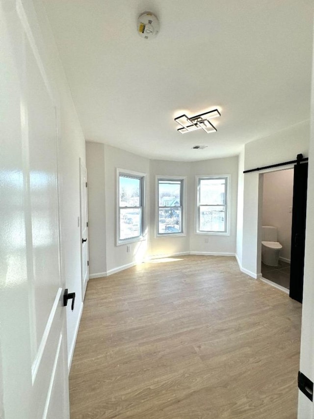 spare room featuring a barn door, light wood-type flooring, and baseboards