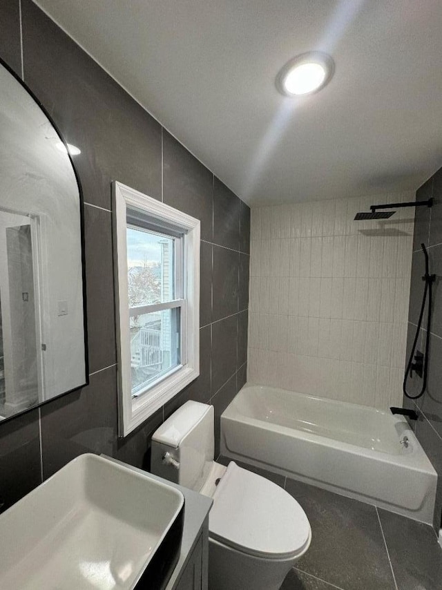 full bathroom featuring toilet, tile patterned floors, vanity, washtub / shower combination, and tile walls