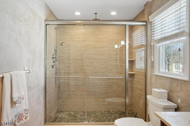 bathroom with tile walls, vanity, toilet, and a shower stall