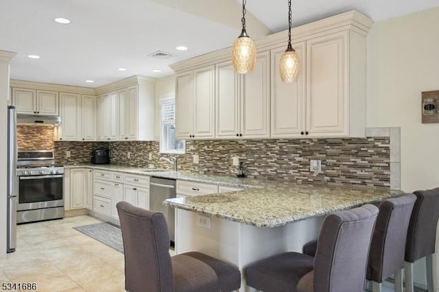 kitchen with pendant lighting, stainless steel appliances, a peninsula, light stone countertops, and under cabinet range hood