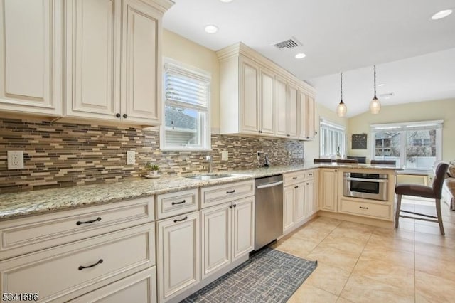 kitchen featuring appliances with stainless steel finishes, a peninsula, a sink, cream cabinets, and a wealth of natural light