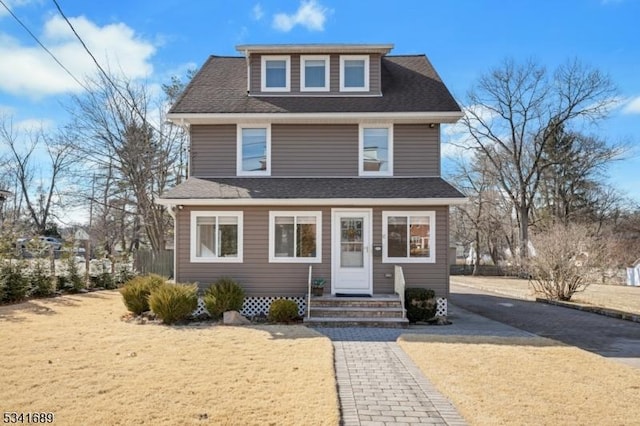 traditional style home with a shingled roof, entry steps, and a front lawn