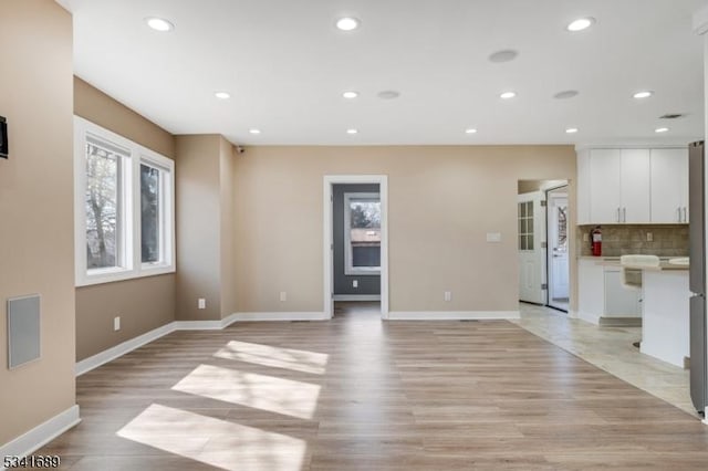 unfurnished living room with a healthy amount of sunlight, light wood-style floors, baseboards, and recessed lighting