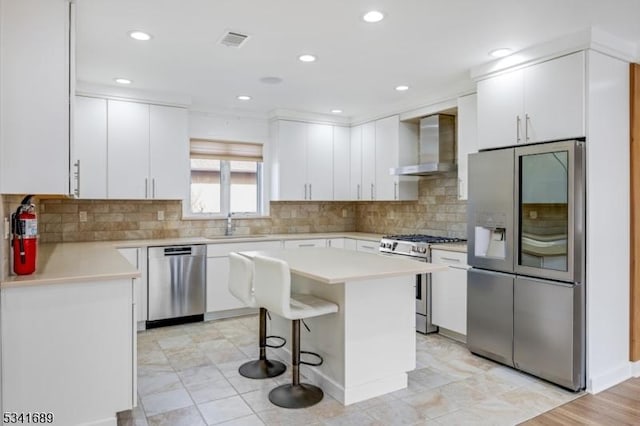 kitchen featuring a breakfast bar area, stainless steel appliances, light countertops, white cabinets, and wall chimney range hood