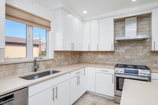 kitchen with tasteful backsplash, light countertops, appliances with stainless steel finishes, a sink, and wall chimney exhaust hood