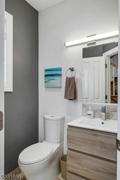 half bath featuring toilet, backsplash, and vanity