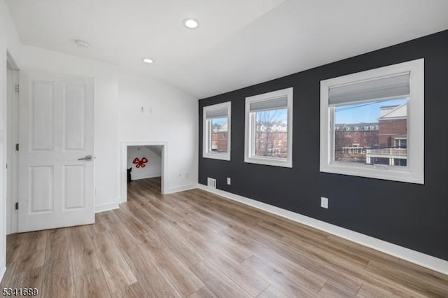 spare room featuring light wood-type flooring, lofted ceiling, baseboards, and recessed lighting