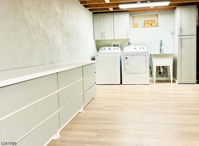 clothes washing area featuring separate washer and dryer, light wood-style flooring, and cabinet space