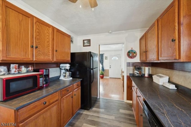 kitchen featuring dark countertops, black appliances, brown cabinetry, and wood finished floors