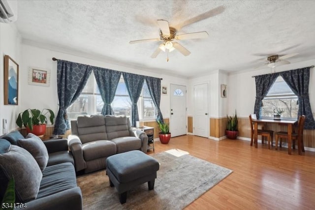 living room with a ceiling fan, wainscoting, wood finished floors, a wall mounted air conditioner, and a textured ceiling