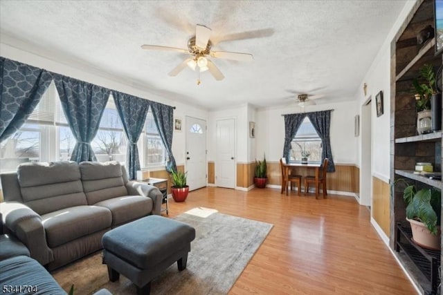 living room featuring a wainscoted wall, a ceiling fan, a textured ceiling, and wood finished floors